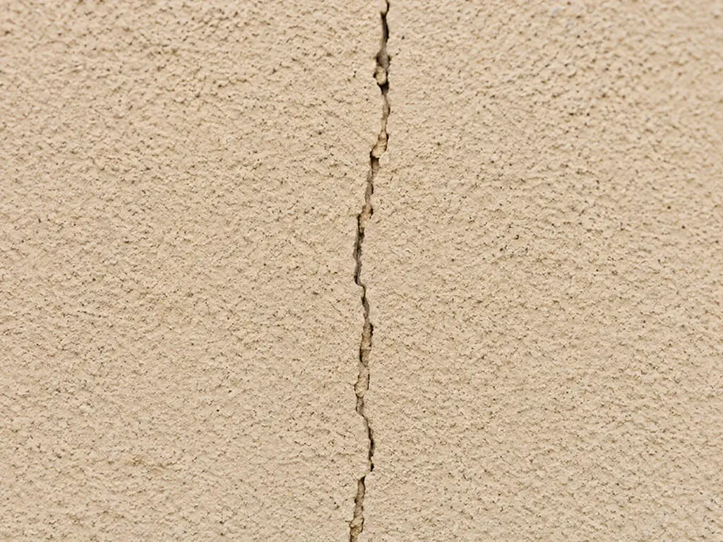 Fissure fine verticale traversant l'enduit d'un mur